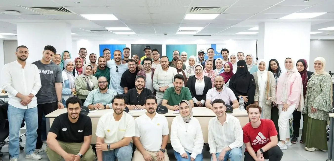A group photo: around fifty participants and mentors in a training room, smiling at the camera.