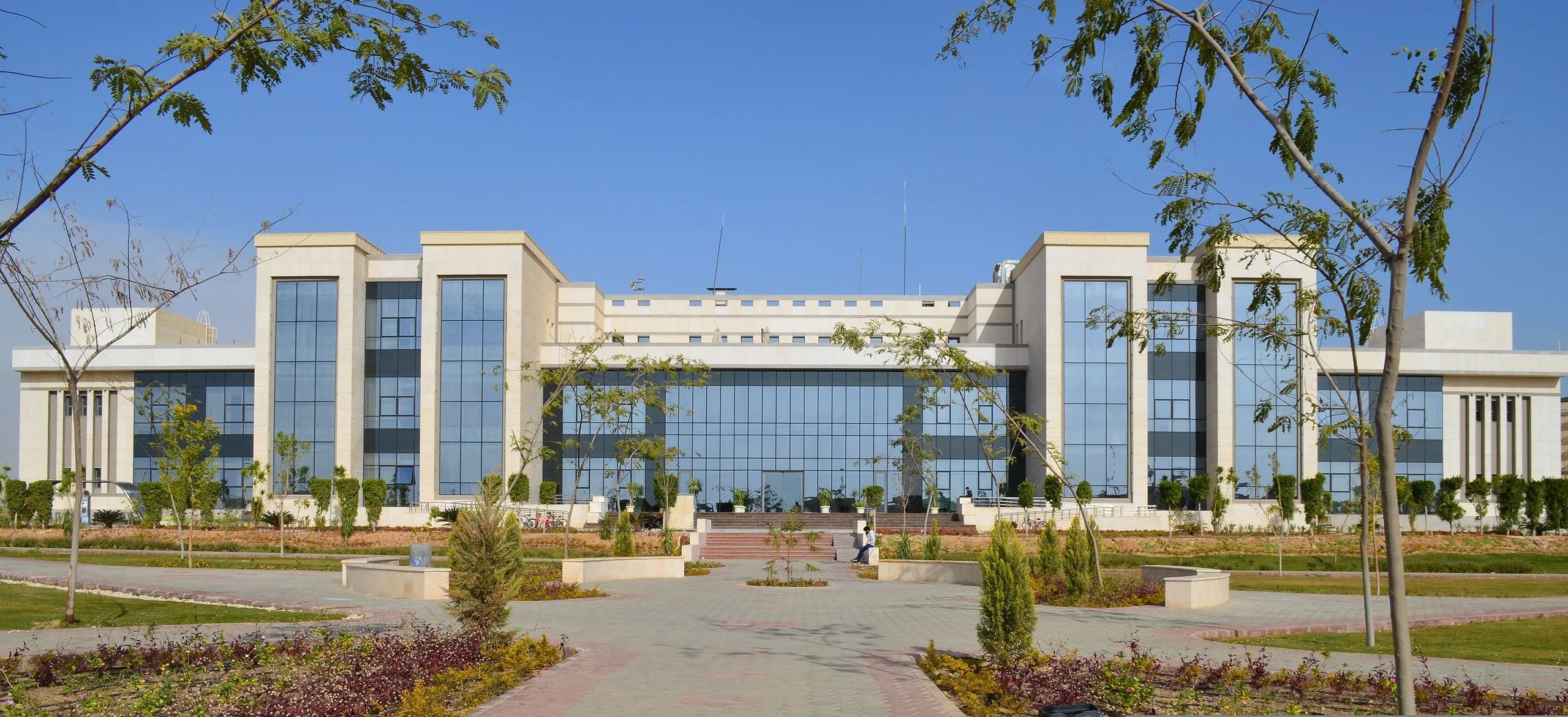 The main building at Zewail City, a long glass-and-stone front under a clear blue sky.