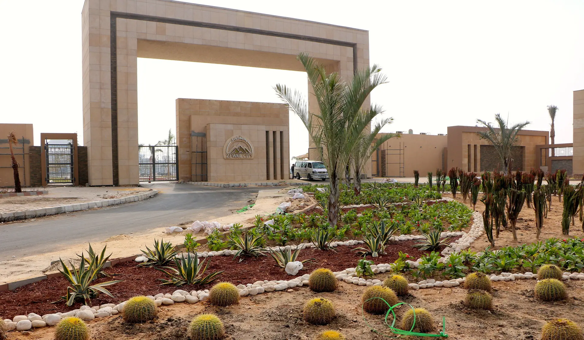 The Zewail City gates: a tall sandstone arch and gatehouse, with a cactus garden in front.